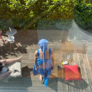 Eine Person in einem blauen Elefantenkostüm ist aus der Vogelperspektive fotografiert. Sie steht auf einer hölzernen Terrasse und blickt zur Kamera hinauf.