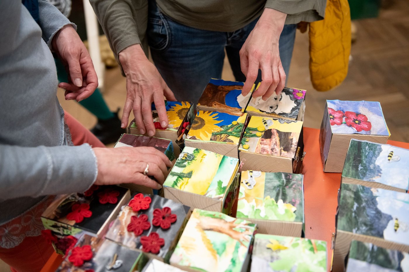 zwei Personen halten ihre Hände über Holzwürfel auf denen verschiedene gemalte Abbildungen von Planzen zu sehen sind, die aneinandergereiht ein Bild ergeben