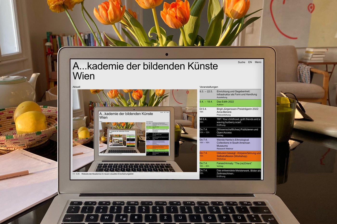 Foto eines Schreibtisches mit Laptopbildschirm in der Mitte, im Hintergrund gelbe Tulpen