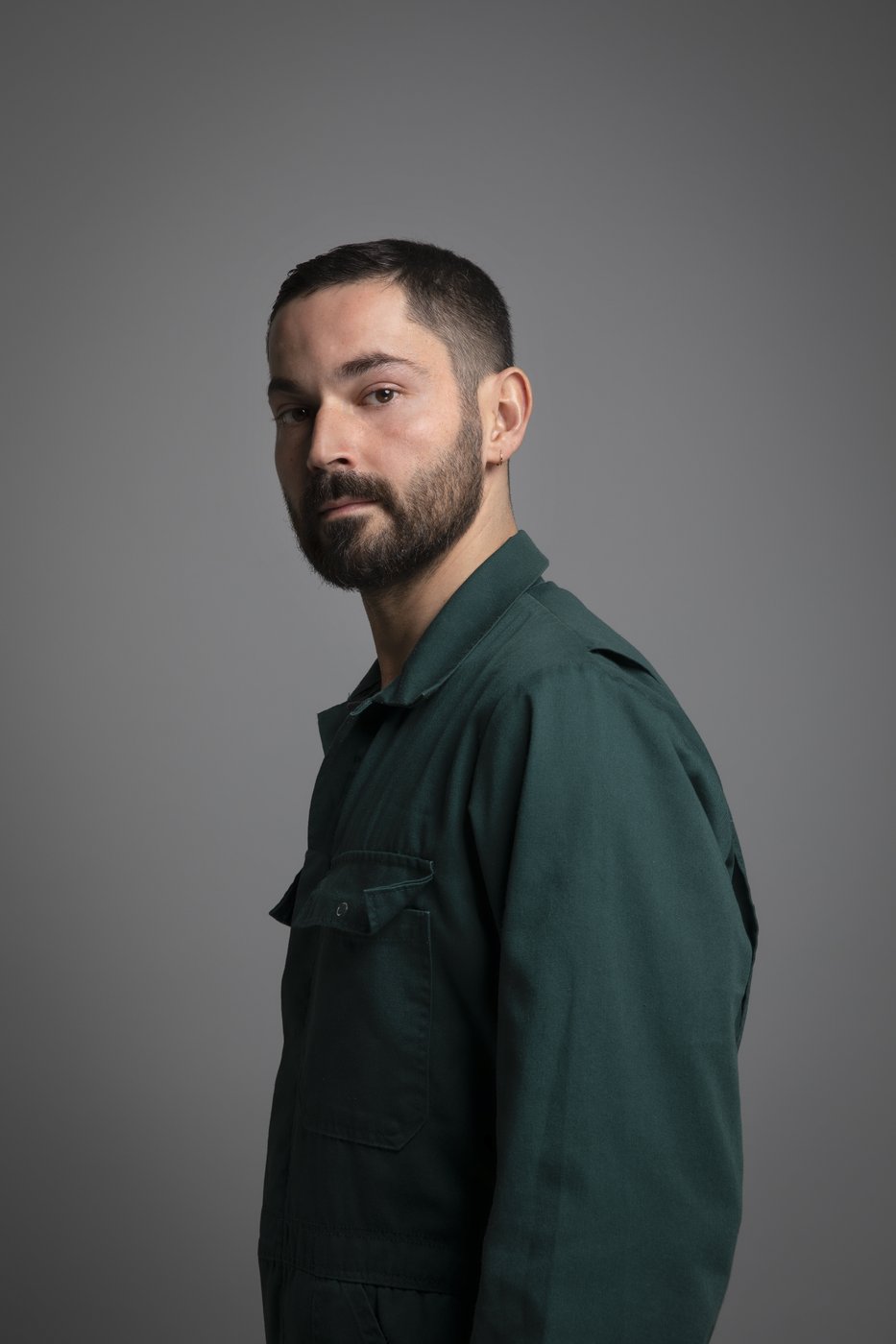 Der Künstler Aykan Safoğlu steht in einem grünen Hemd vor einem grauen Hintergrund.