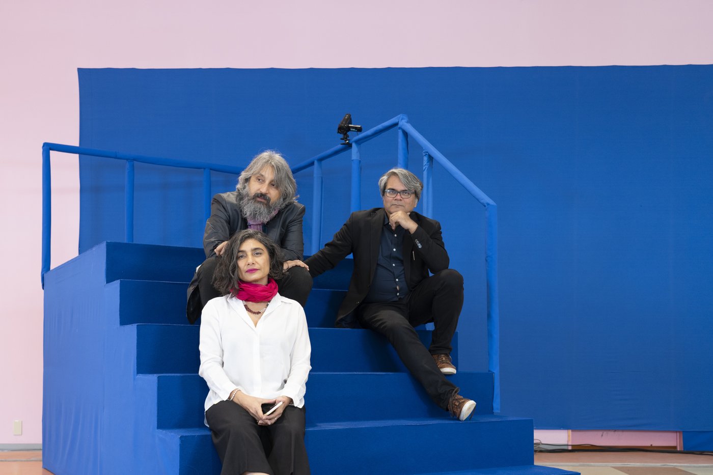 Foto von drei Personen, die auf einer blauen Treppe vor blauem Hintergrund sitzen