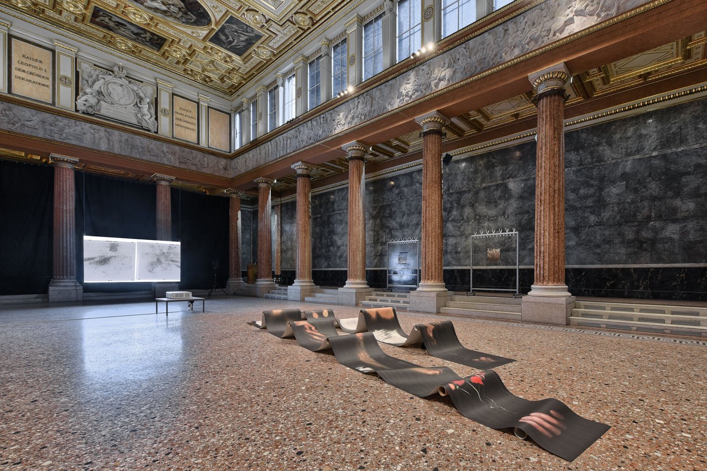 Aula der Akademie mit einer wellenförmigen Papierinstallation und einem Screen im Hintergrund