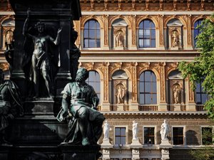 Ausschnitt der Fassade des Akademiegebäudes am Schillerplatz mit einem Ausschnitt des Schillerdenkmals davor