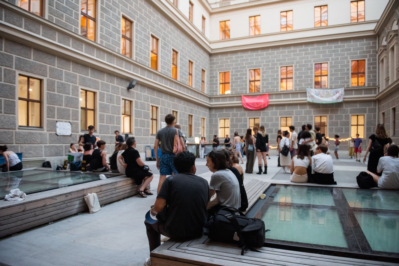 mehrere Personen sitzen und stehen im Innenhof der Akademie und unterhalten sich