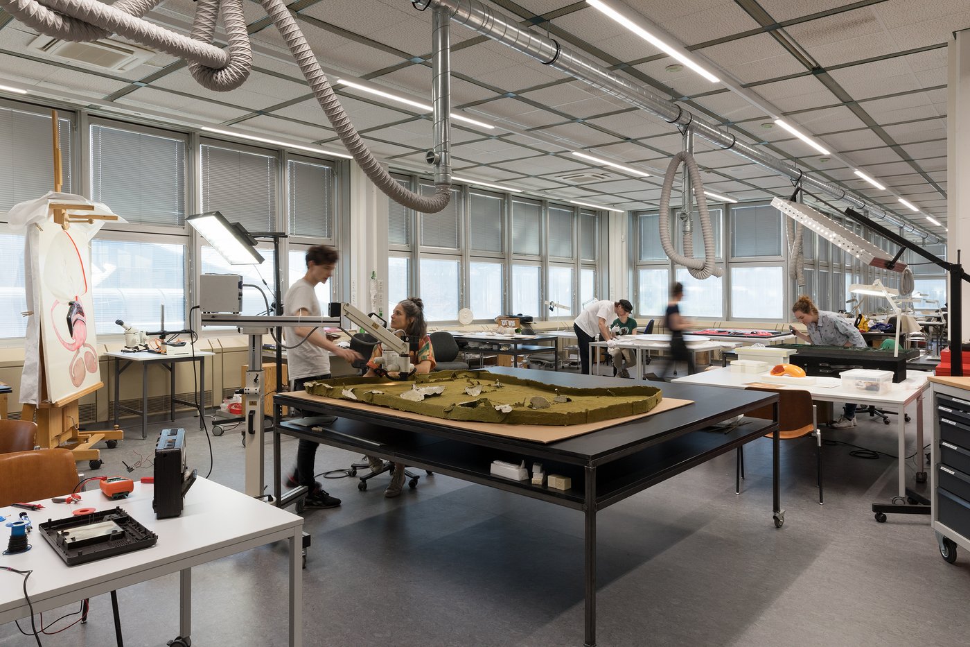 View into a large, bright studio space with several work tables, students working at some.