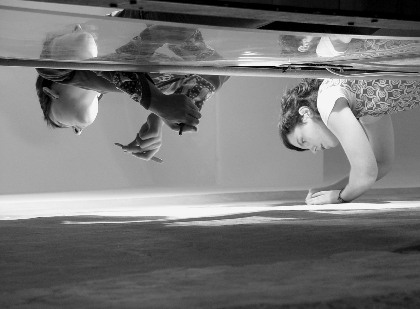 The bw work shot shows two female students with exposure tools in their hands, taken in low perspective. Only the heads and arms or hands are visible. The two are working on a wall painting, which cannot be seen in detail.