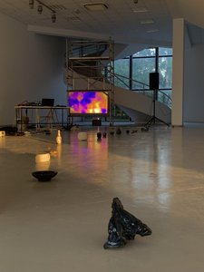 Photo of a showroom with a metal frame on which is a large screen showing a thermal image, in the foreground on the floor small objects lined up.