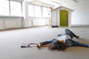 Person on the floor in a room, at the other side a small wooden house with a figure on top