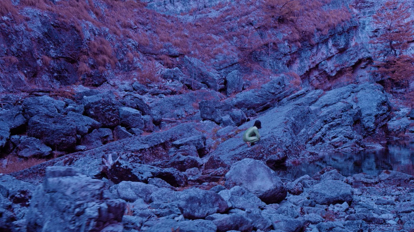 A violet mountain landscape with a tiny cowering female figure.