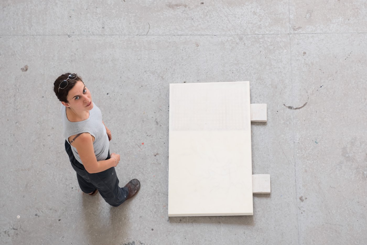 woman standing beside her artwork on the floor and looking up into the camera