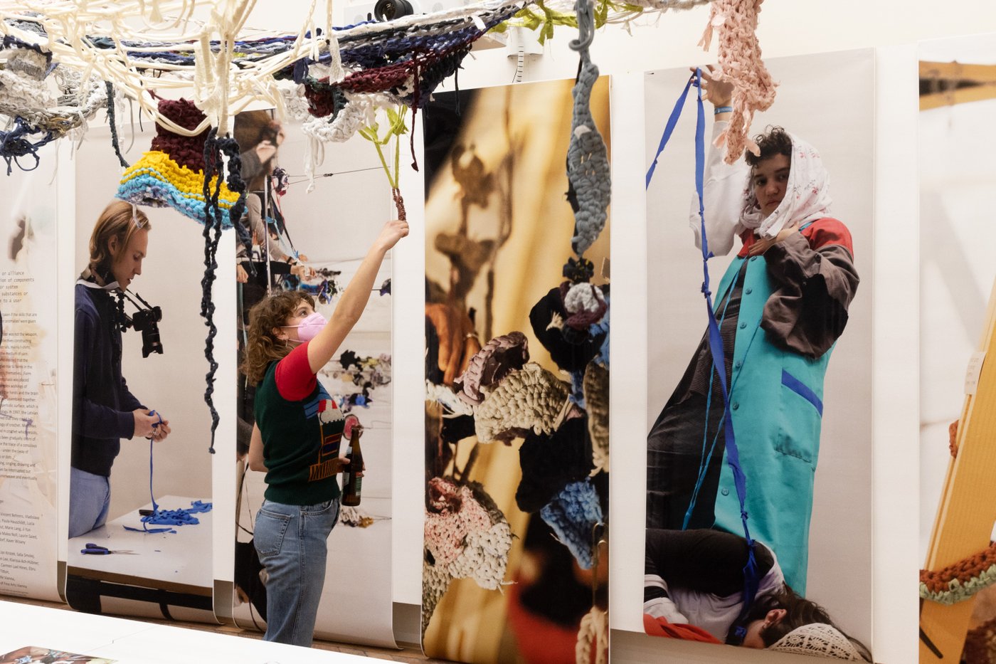 In one room, a net of threads stretches across the ceiling, a person in a mask stands under this tangle of strings and reaches up to grab a string.