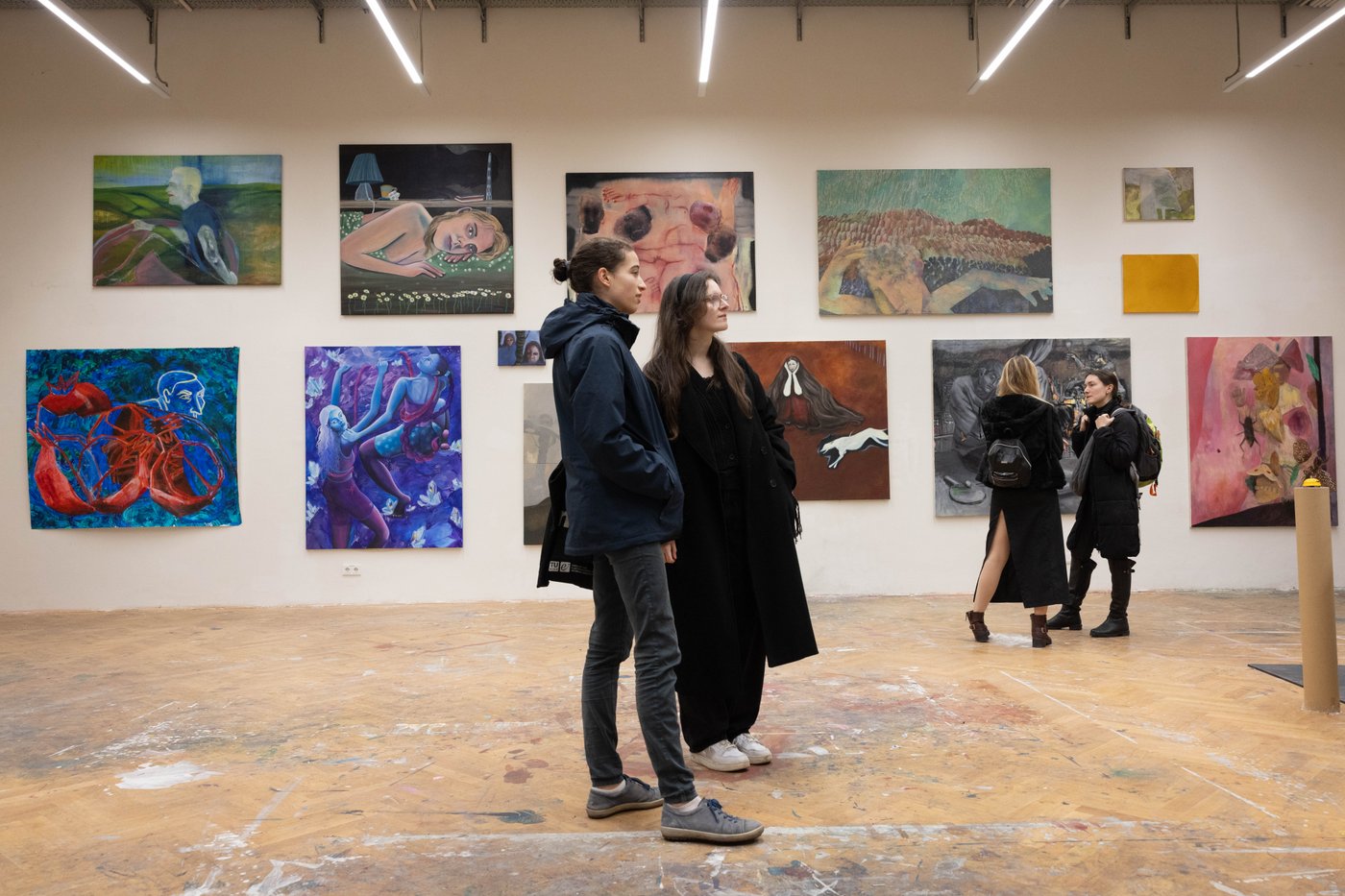 two people in the middle of the picture looking at the art on the walls around them