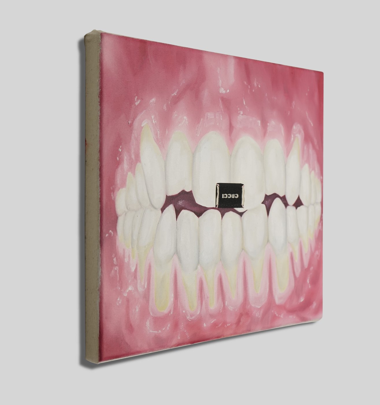 You can see a small-format oil painting, the photo was taken from the side, therefore the canvas appears distorted in perspective. The canvas depicts a format-filling mouth interior presented in an unusual way. The gums as well as all the teeth are clearly visible, the lips seem to be folded back or put over the "lens". In the center of the painting, a label of the Gucci fashion brand has been turned inside out and sewn on