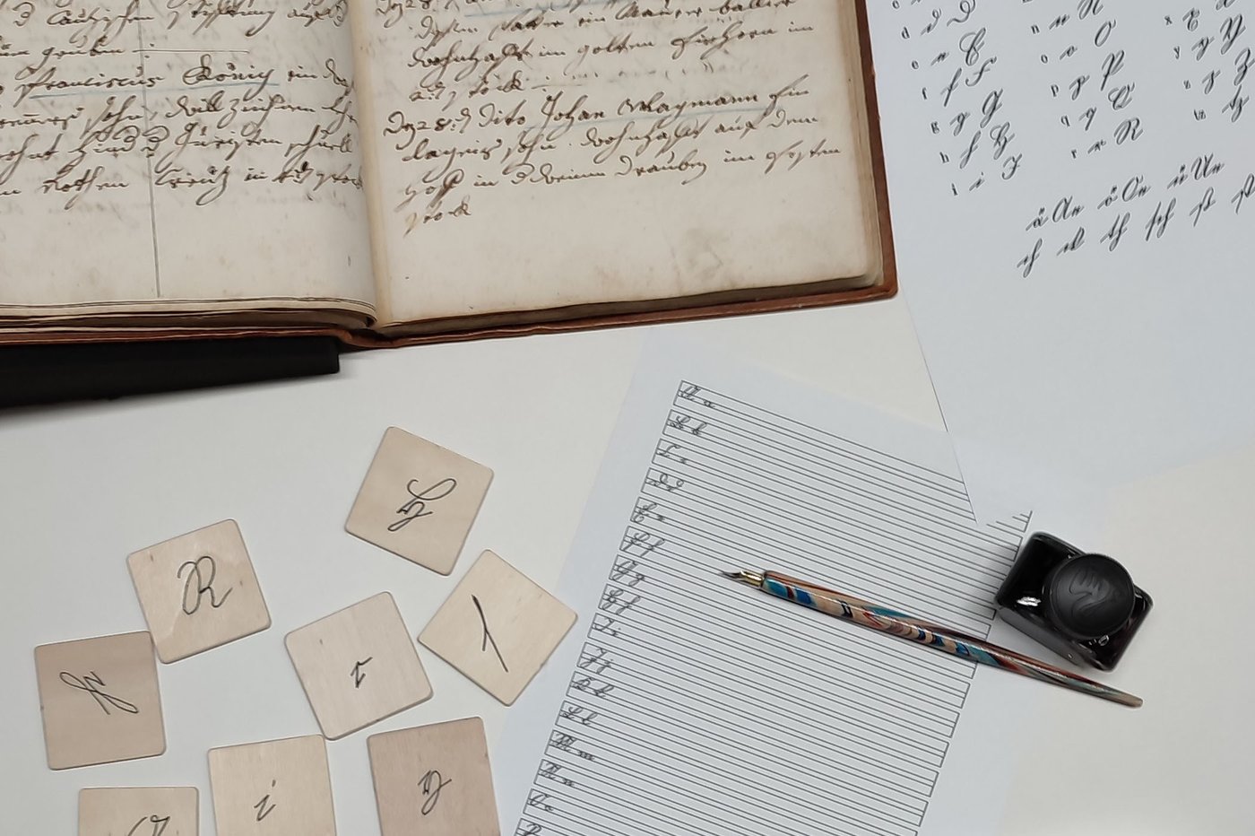 Top left: Matriculation register from the holdings of the university archive of the Academy of Fine Arts Vienna, 1754–1769/72; top right: Kurrent alphabet; bottom left: Kurrent memory cards; bottom right: Practice sheet, quill with steel nib, glass inkwell