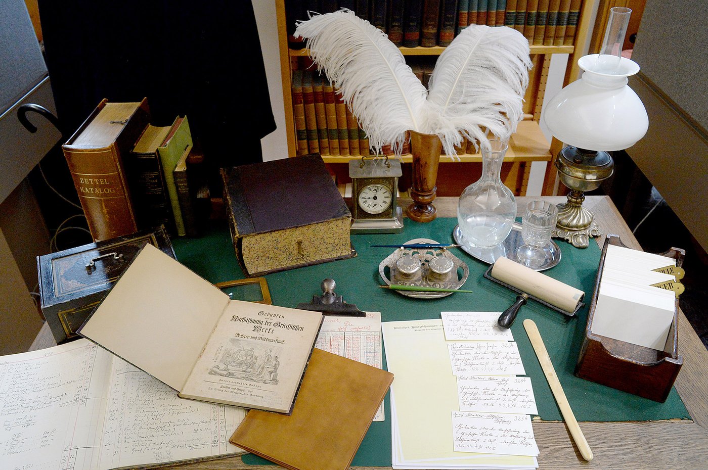 The color photograph shows what may be a typical desk or work table of a senior official in the library service. A scriptor or an amanuensis (assistant scribe) possibly, since these two people with this job title have to do the work of the classic "librarian" behind the scenes. In addition to the necessary work utensils – such as nib pens, inkwell, blotting cradle, index cards, and various inventory books and lists – the everyday work is completed by many other period-typical accessories, which allows you to put yourself in the necessary work steps and to revel and live a little in the flair of the 19th century.