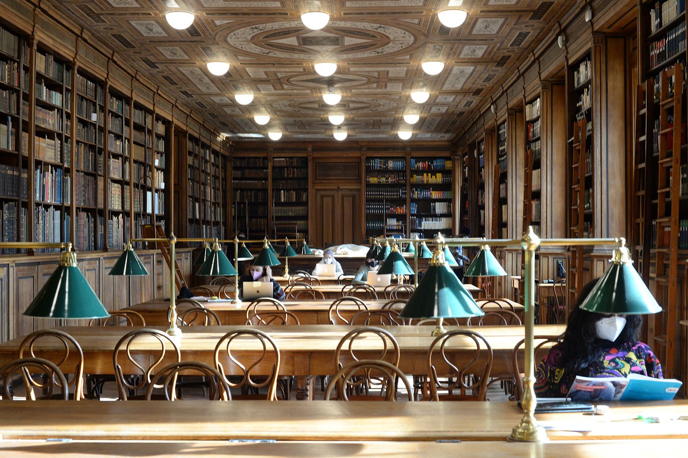 Readers in the reading room with laptops and FFP2 masks. The sun is shining and illuminating the tables.